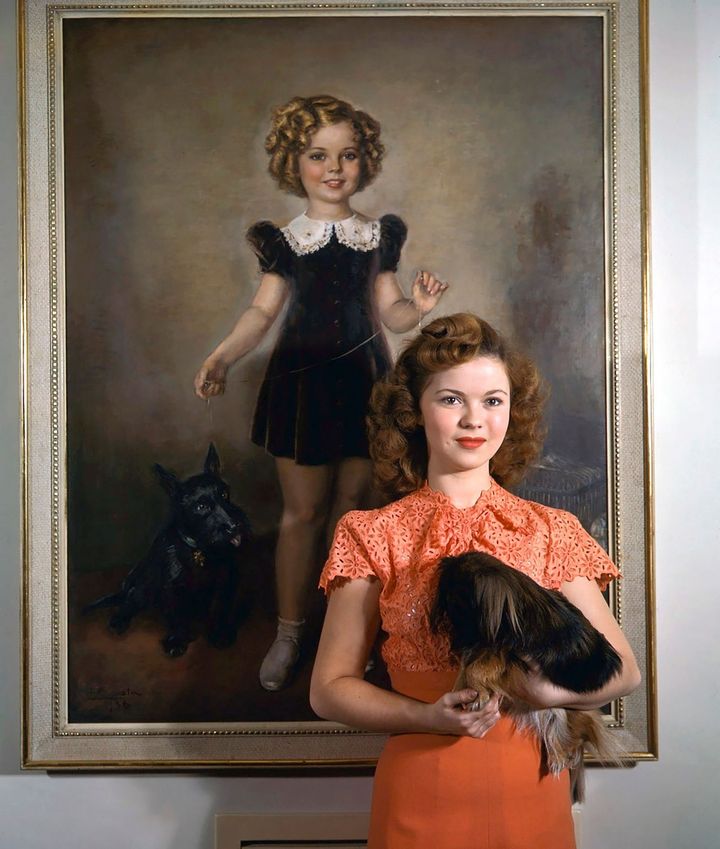 Shirley Temple posant devant un tableau d'elle-même quand elle était jeune enfant 1945